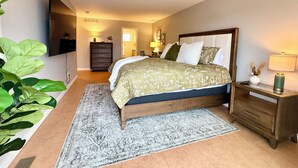 Une chambre à coucher comprenant un lit, des tables de chevet, une commode, un téléviseur fixé au mur et une grande plante.