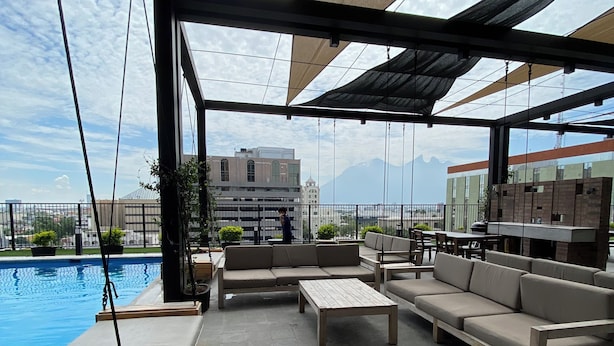 A rooftop terrace with outdoor seating, a swimming pool, and a view of distant mountains.