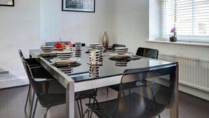 Une table à manger dressée avec des assiettes, un vase et une fenêtre avec des stores.