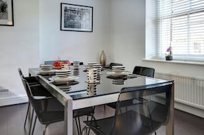 Une table à manger dressée avec des assiettes, un vase et une fenêtre avec des stores.