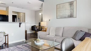 A modern living room with a sofa, coffee table, and a dining area with a table and chairs. - Canal Walk District Apartments by Landing (Indianapolis)