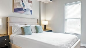 A neatly made bed with a headboard, two bedside tables with lamps, and a window with blinds. - Canal Walk District Apartments by Landing (Indianapolis)