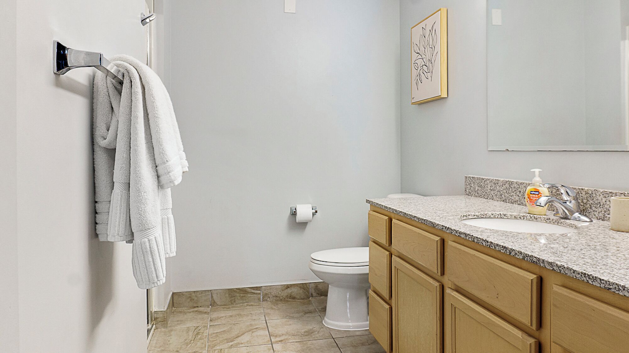 A bathroom with a toilet, a sink with a soap dispenser, and a towel rack with multiple towels.