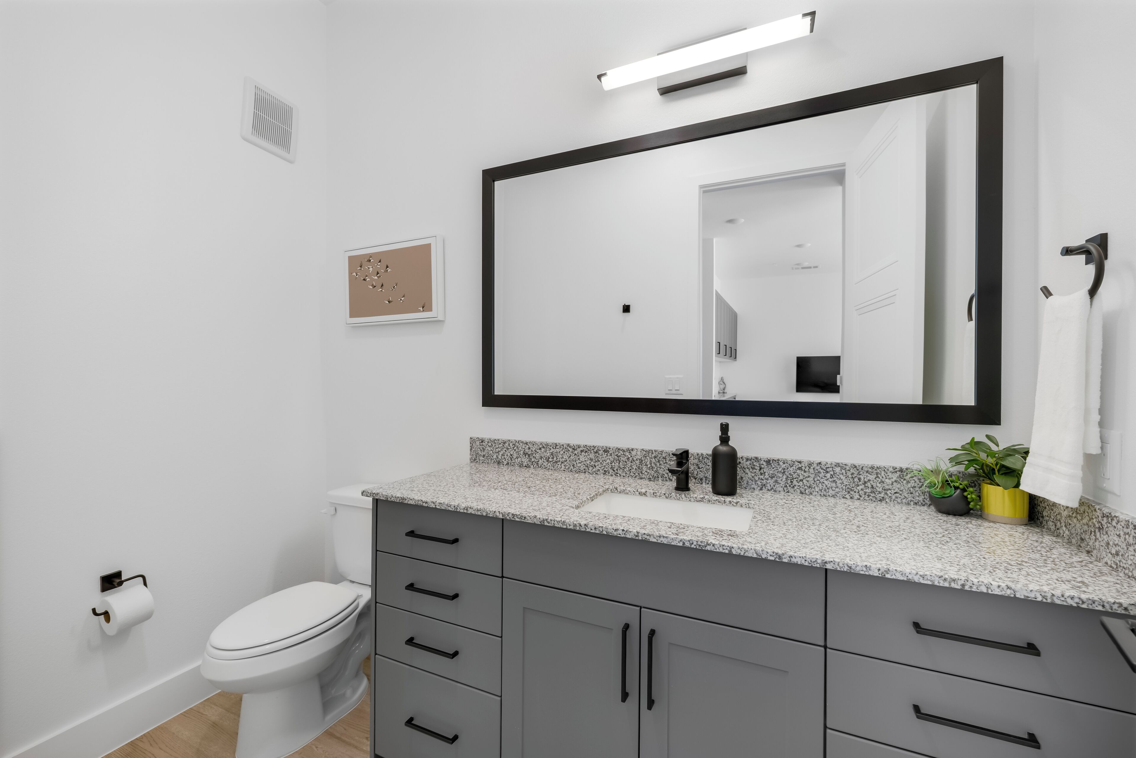 Ein modernes Badezimmer mit Toilette, einer Granit-Arbeitsplatte, einem großen Spiegel und einem Waschbecken.