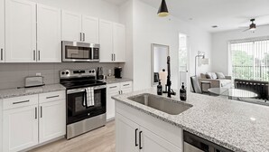 A modern kitchen with white cabinetry, stainless steel appliances, a granite countertop, and a large window overlooking a balcony. - Landing Apartments Denton (Denton)