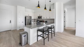 A modern kitchen with white cabinets, stainless steel appliances, and a central island with bar stools. - Landing Apartments Denton (Denton)