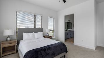 A bedroom with a bed, bedside tables, a ceiling fan, and a view into the kitchen.