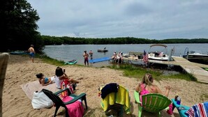 A beach with people relaxing on chairs and a dock with boats. - Large, Family-Friendly Lake Home, On Snowmobile/ATV Trails, W/D, Firepit (Harshaw)