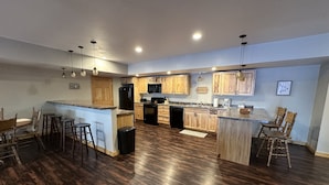 A spacious kitchen with wooden cabinets, a central island, and bar stools. - Large, Family-Friendly Lake Home, On Snowmobile/ATV Trails, W/D, Firepit (Harshaw)