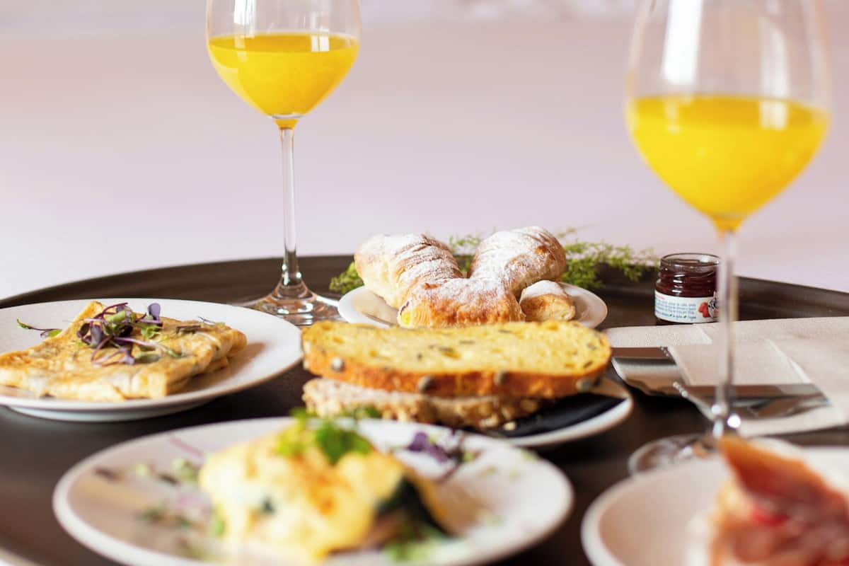 Ett brickbord med olika rätter och glas med apelsinjuice står på ett bord i ett hotellrum.