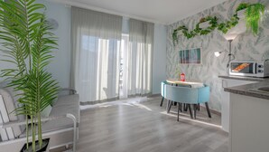 Una sala moderna con sofá, una mesa de comedor con sillas, un área de cocina con microondas y una planta grande en maceta.