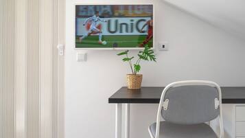 A modern room with a TV mounted on the wall displaying a soccer match, a small potted plant on a table, and a grey chair.