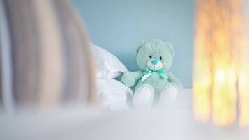 Un osito de peluche verde sobre una cama con almohadas blancas y una pared azul al fondo.