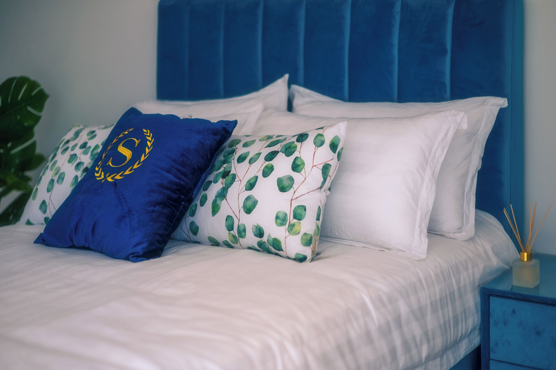 A bed with white bedding and two pillows, one blue and one with a green leafy pattern.