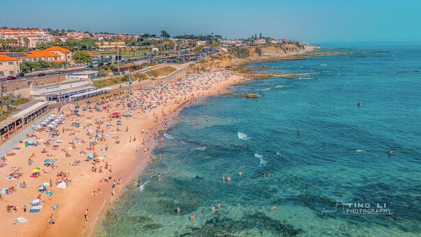 Una playa con agua azul cristalina, una orilla de arena y un paisaje urbano al fondo.