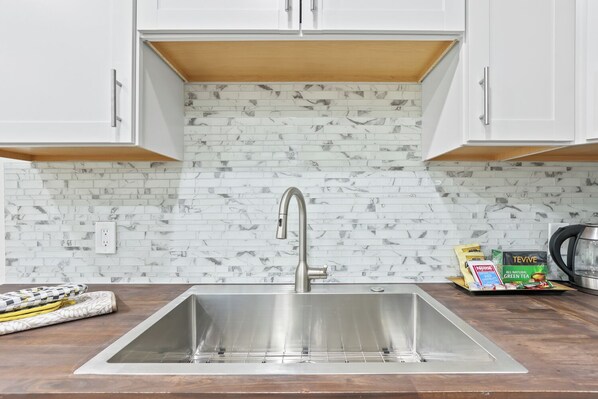 A kitchen with a stainless steel sink, white cabinets, and a marble-patterned backsplash.