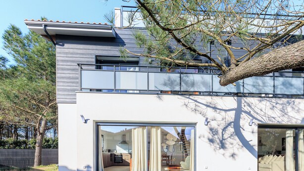 Une maison moderne dotée d’une grande porte-fenêtre coulissante, d’un balcon et d’une pelouse bien entretenue.