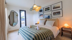 Une chambre à coucher avec un lit, une table de chevet, une lampe, un miroir et des tableaux encadrés accrochés au mur.