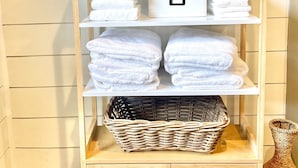 A wooden shelf with white towels, a wicker basket, and a vase with green foliage.