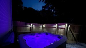 A hot tub with a blue light, surrounded by wooden fences and a wooden deck.
