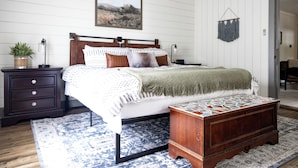 A bedroom with a bed, a nightstand, a dresser, a rug, and a wall-mounted macrame piece.