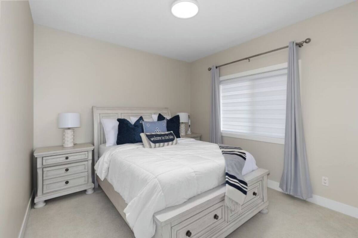 Un dormitorio con cama, mesitas de noche, una ventana con cortinas y una lámpara en el techo.