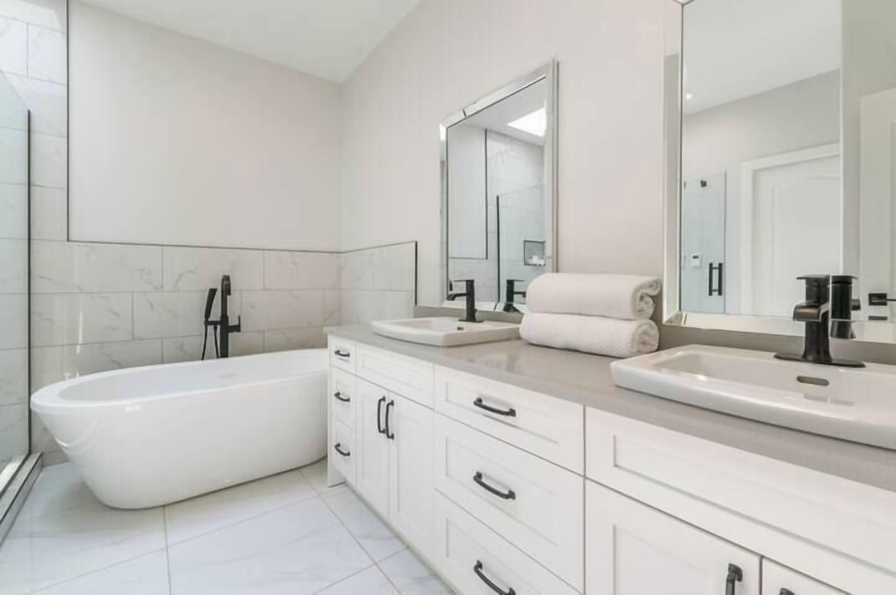 A modern bathroom with a freestanding bathtub, two sinks, and a large mirror.