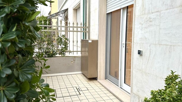 Un espace extérieur carrelé, agrémenté d’un portail en métal, d’une porte-fenêtre coulissante et d’une petite plante en pot.