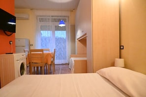 Ein Hotelzimmer mit Bett, Tisch mit Stühlen, Waschmaschine, Fernseher und einem Fenster mit Vorhängen.