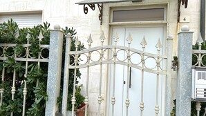 Une entrée fermée par un portail, avec une porte blanche, une plaque portant le numéro « 4 » et un portail en métal agrémenté d’éléments décoratifs.