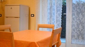 Une pièce comprenant une table, deux chaises, un réfrigérateur et une fenêtre avec des rideaux.