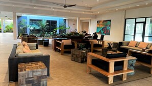 A spacious lobby with a variety of seating options, including sofas and chairs, arranged around a central coffee table. There is a large window providing natural light and a view of the outdoors.