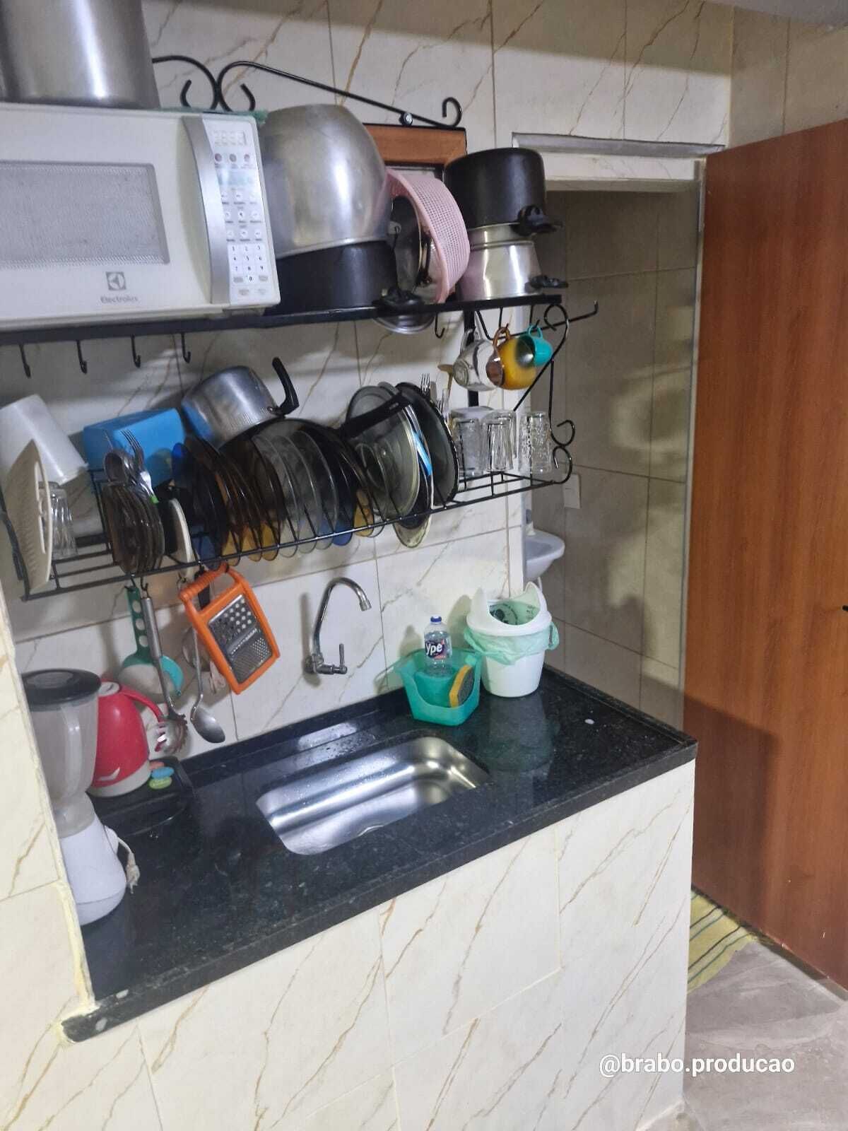 A kitchen with a black countertop, a sink, and various kitchen utensils and appliances like a microwave, kettle, and pots.