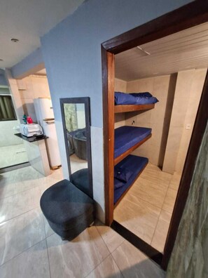 Una stanza con un letto a castello, una piccola area salotto, uno specchio e un angolo cottura con bollitore.