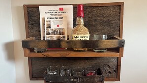 Una estantería de madera con un folleto de roble bourbon, una botella etiquetada 'Maker's Mark' y vasos.