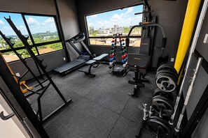 Een sportschool met een loopband, bankdrukrek, gewichtrek en dumbbells.