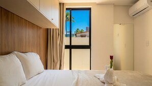 A hotel room with a bed, a window with a view, a door, and an air conditioning unit. - Foot in the sand in Porto de Galinhas (Ipojuca)