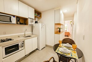 Cocina compacta con microondas, estufa, horno y refrigerador. Hay una mesa de comedor con platos y un vaso.