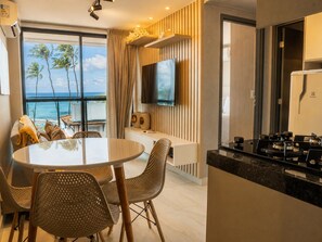 A modern kitchen with a round dining table, wicker chairs, and a view of the ocean. - Luxury flat on the sand (Ipojuca)