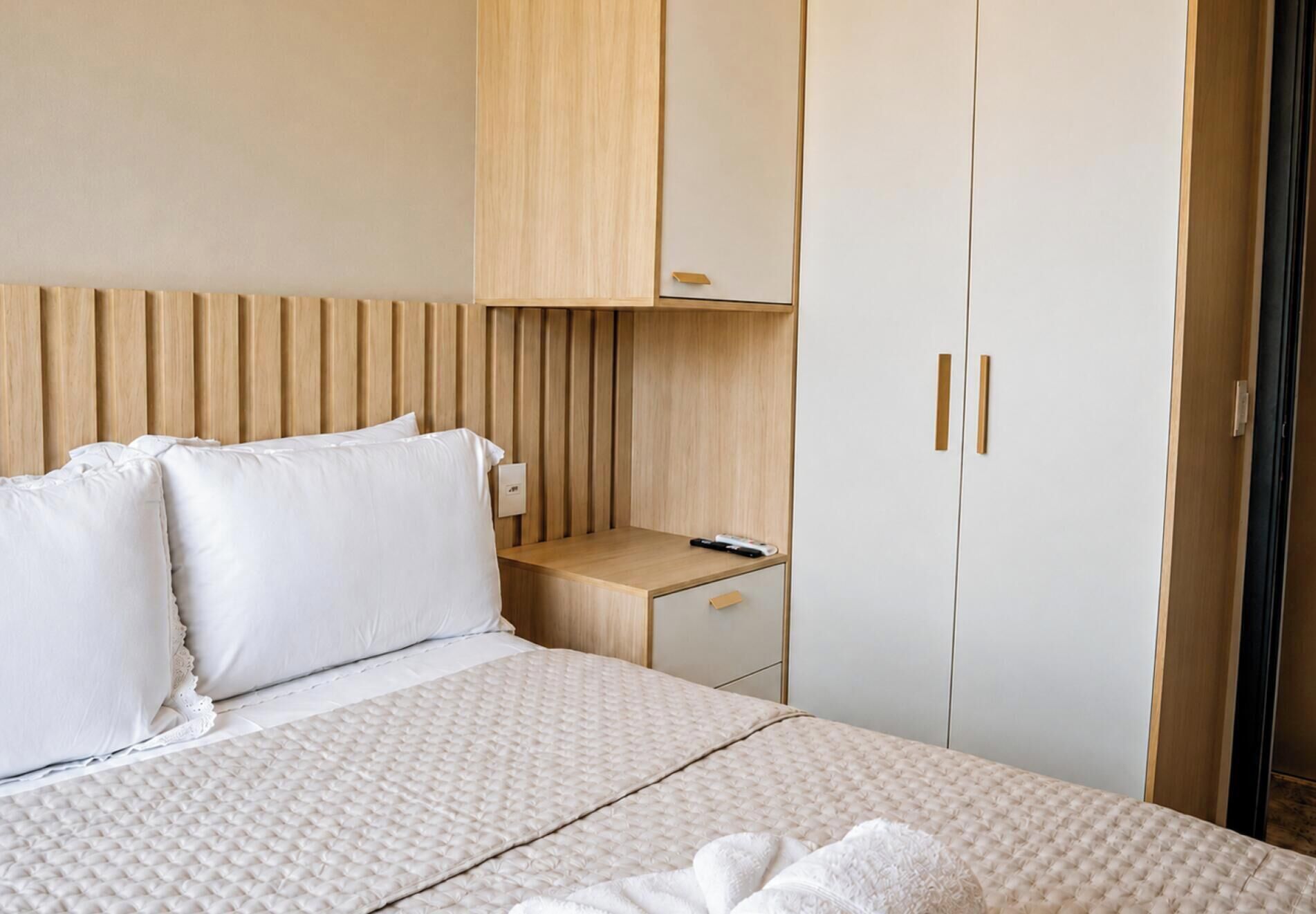 Una habitación de hotel con cama, mesita de noche de madera, escritorio y armario.
