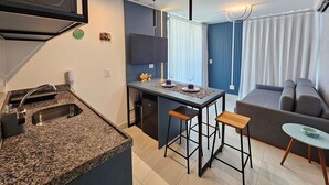 A modern kitchen with granite countertops, a built-in oven, and a dining area with a bar stool and a small table. - Amazing flat on the sand (Ipojuca)