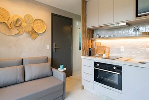 A modern kitchen with built-in appliances, a grey sofa, and decorative wall art. - Cozy and complete flat (Ipojuca)