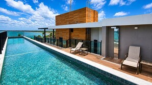 A modern poolside area with a clear view of the ocean, a wooden deck, and a pool. - Flat 301 Makadamia Beachfront (Ipojuca)