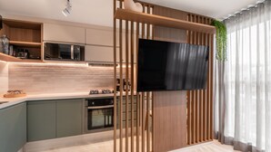 A modern kitchen with built-in appliances, a large flat-screen TV, and a wooden partition with a hanging plant. - Flat 301 Makadamia Beachfront (Ipojuca)