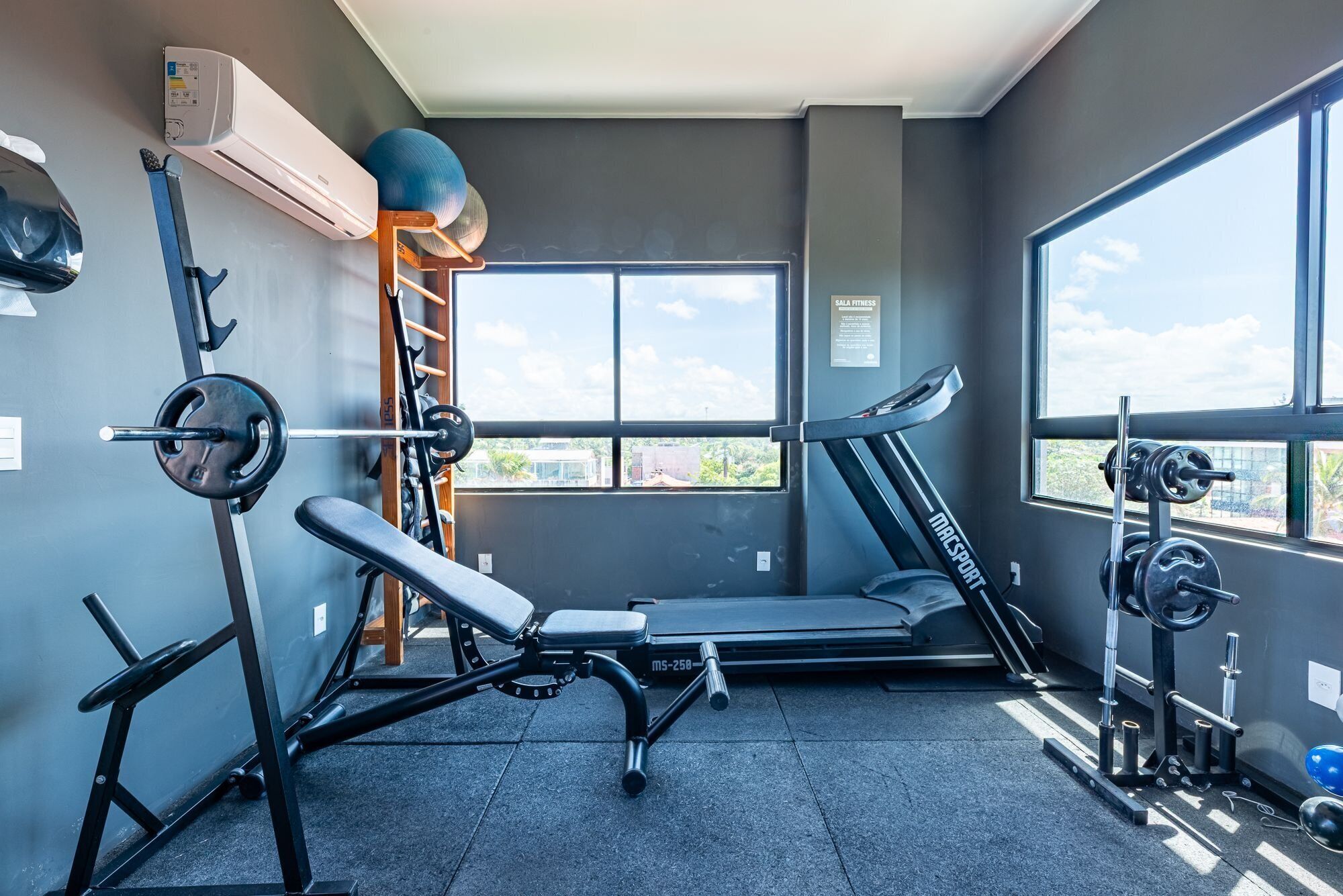 Une salle de sport équipée d’un banc de développé couché, d’un tapis de course et de supports à poids.