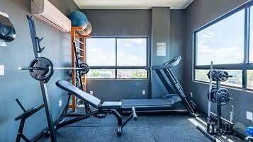 Une salle de sport équipée d’un banc de développé couché, d’un tapis de course et de supports à poids.