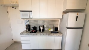 A compact kitchen with white cabinets, a built-in microwave, a coffee maker, and a refrigerator. - 2BR Apartment in Porto de Galinhas | Near Beach (Ipojuca)