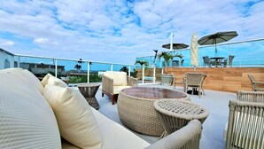 A rooftop terrace with wicker furniture, a round table, and umbrellas. - 2BR Apartment in Porto de Galinhas | Near Beach (Ipojuca)