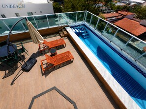 A rooftop pool area with lounge chairs, a table, and a glass balustrade. - Luxury Apartment Near Porto's Natural Pools (Ipojuca)
