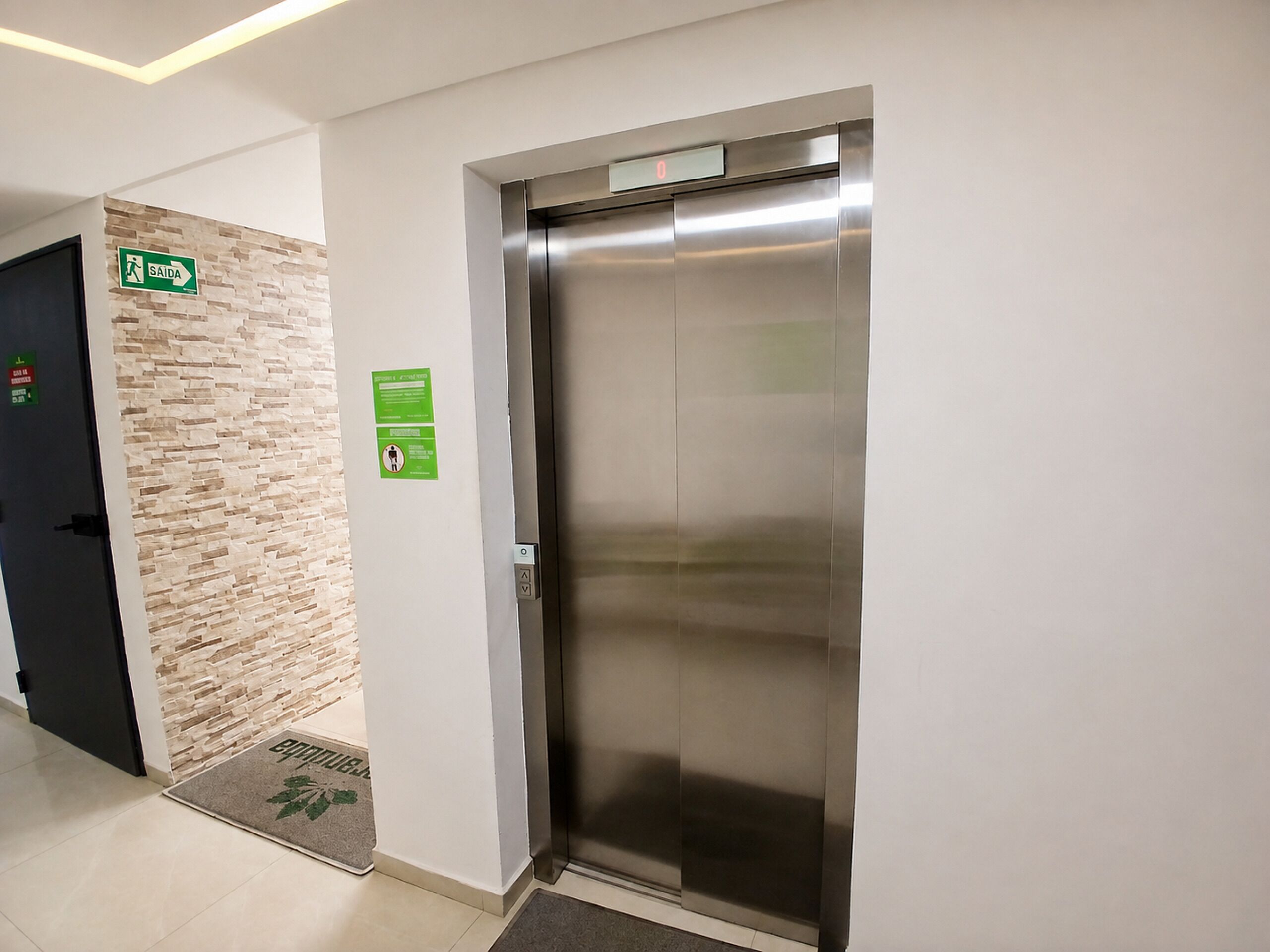 En elevator med et digitalt display, et fastgjort nødudgangsskilt og en dør med et grønt sikkerhedssymbol.